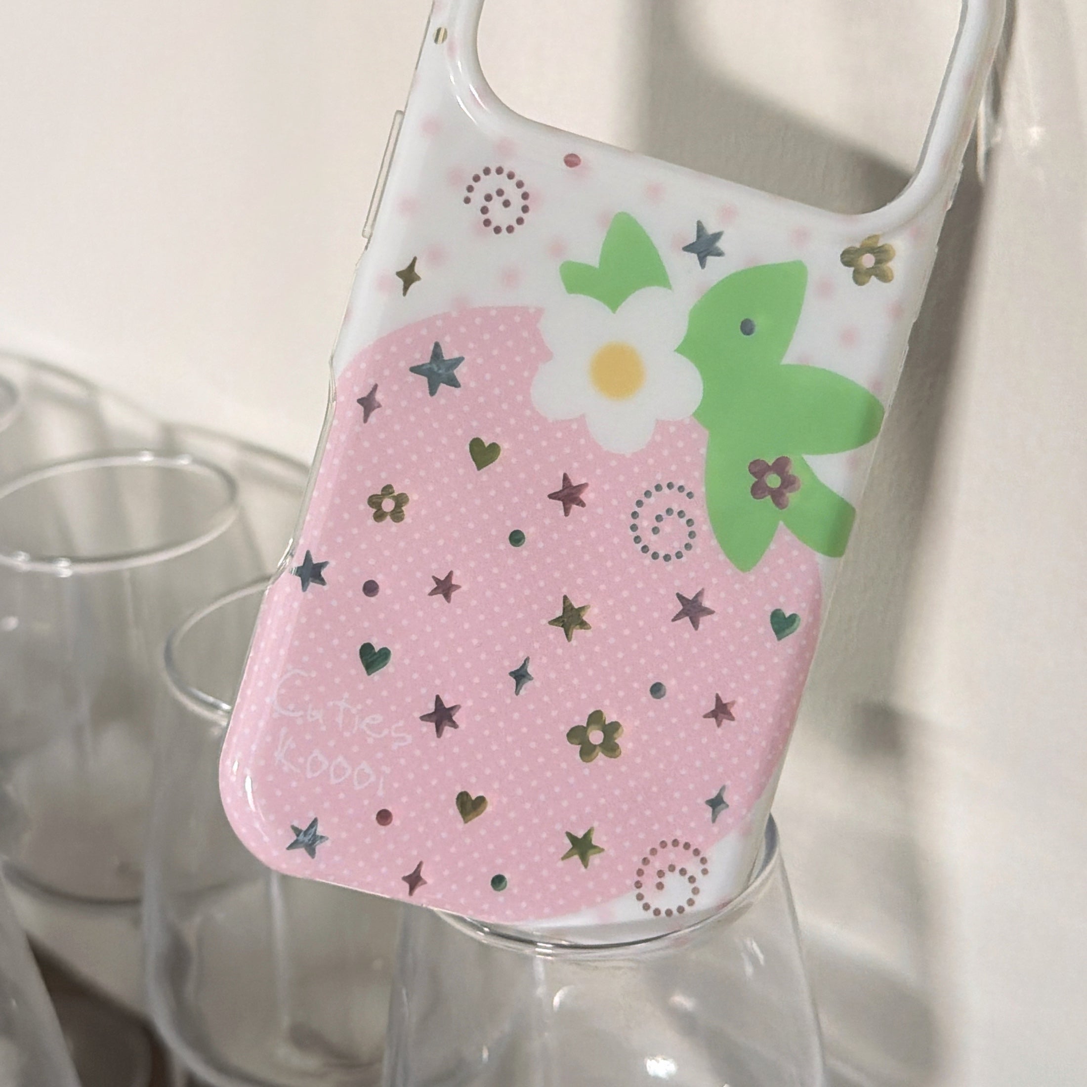 Close-up detail of a holographic glitter star pink strawberry phone case resting on clear glass cups.
