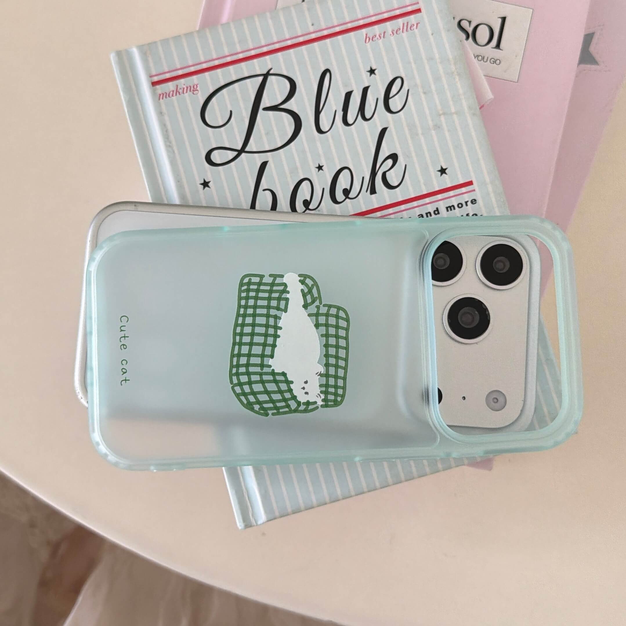 A horizontal view of a clear lazy cat iPhone case resting on a blue book.