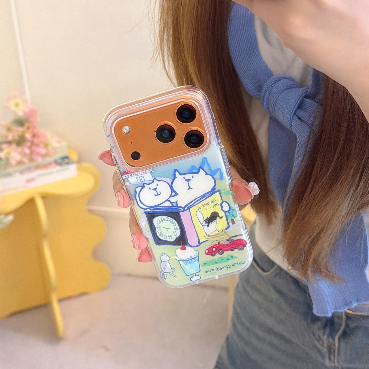 A hand showing a clear graphic phone case with a colorful Japanese doodle art print on a bronze-colored iPhone.