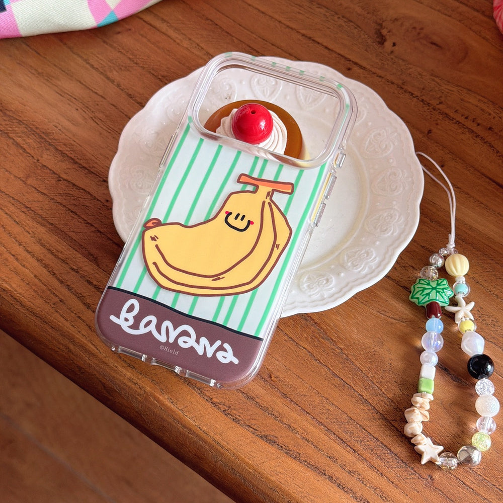 A clear cute banana striped phone case lying on a wooden table next to a decorative dessert plate and a beaded strap.