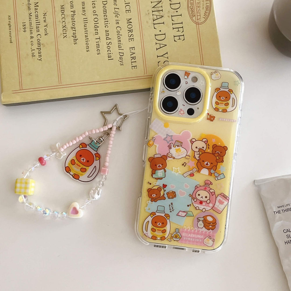 Flat lay of a yellow cartoon bear phone case and its detached colorful beaded keychain lanyard next to an old vintage book.