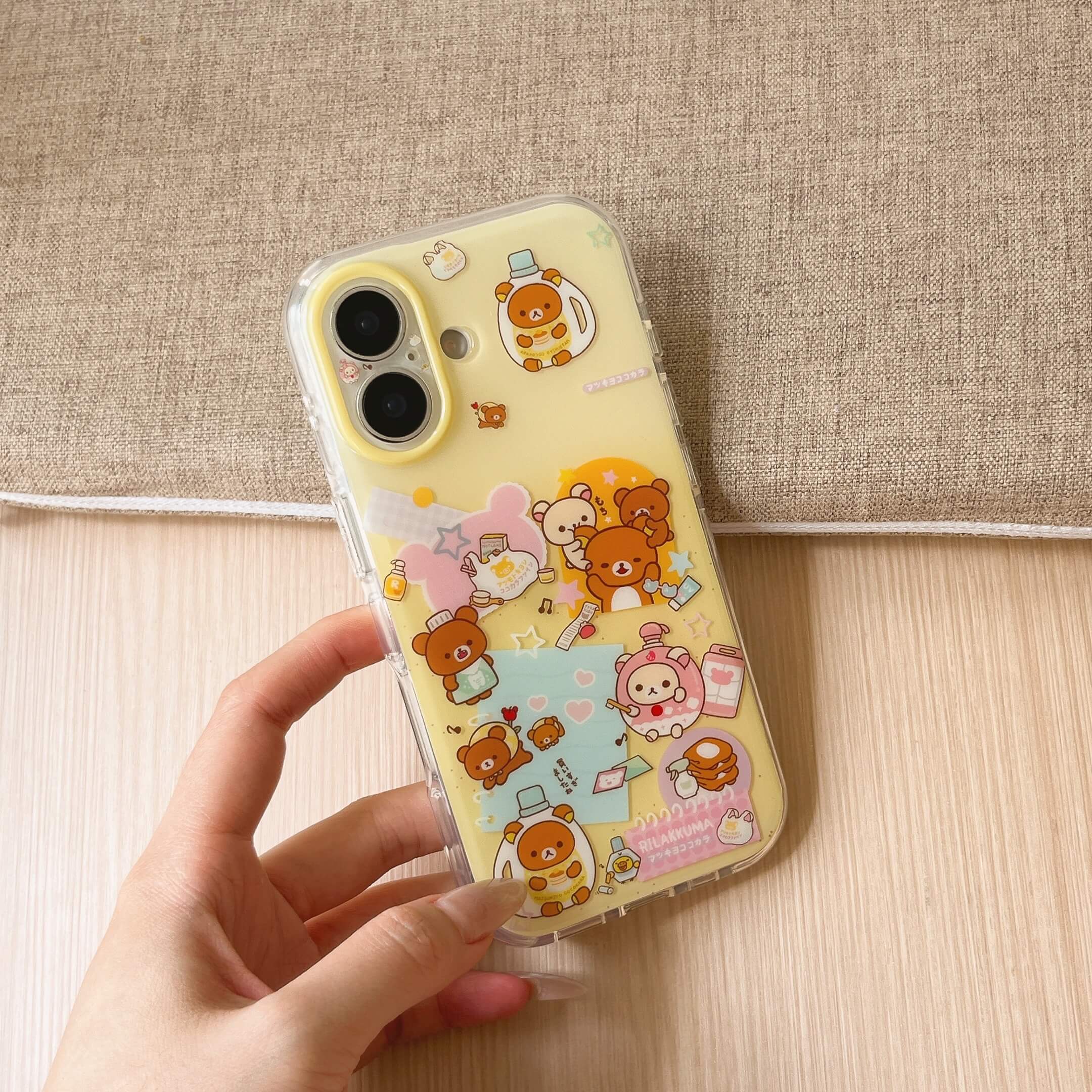 A clear yellow cartoon bear protective phone case resting on a hand with a textured beige fabric backdrop.