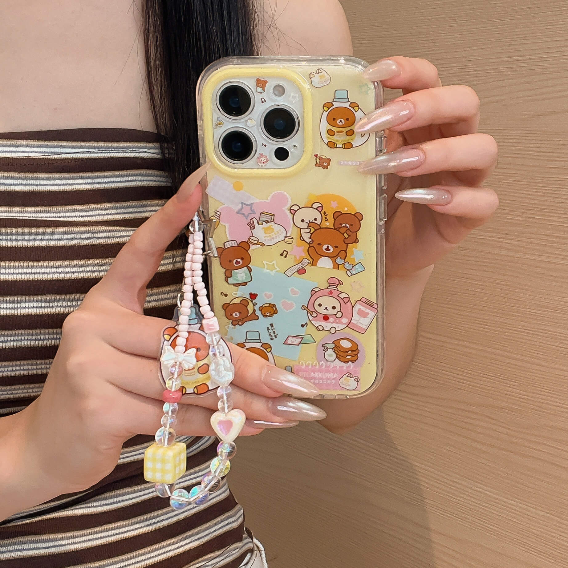 Close-up of a person holding a clear kawaii cartoon bear iPhone case with a yellow camera frame and a beaded star strap.