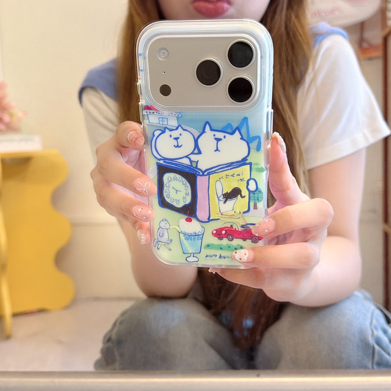 A girl holding a clear iPhone case with a cute hand-drawn white cat illustration for a close-up mirror selfie.