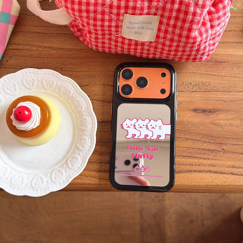 An orange kawaii cat mirror phone case placed flat on a wooden desk next to a sweet pudding dessert.