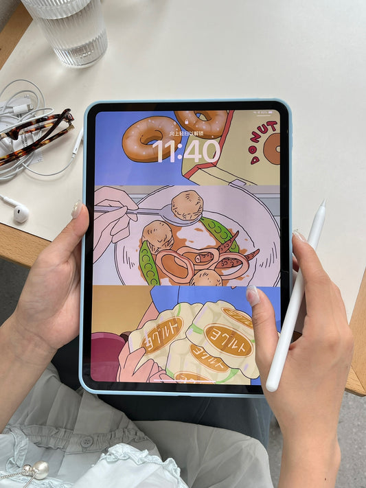 A tabletop flat lay of a kawaii denim print iPad case with a pastel blue bumper frame, surrounded by a white Apple Pencil, wired earphones, and tortoiseshell glasses.