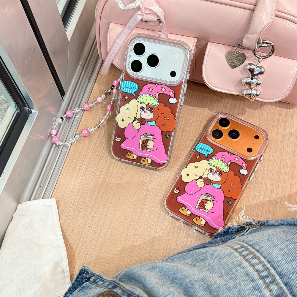 Two kawaii dog eating cookies phone covers displayed on a wooden desk next to a pastel pink handbag.