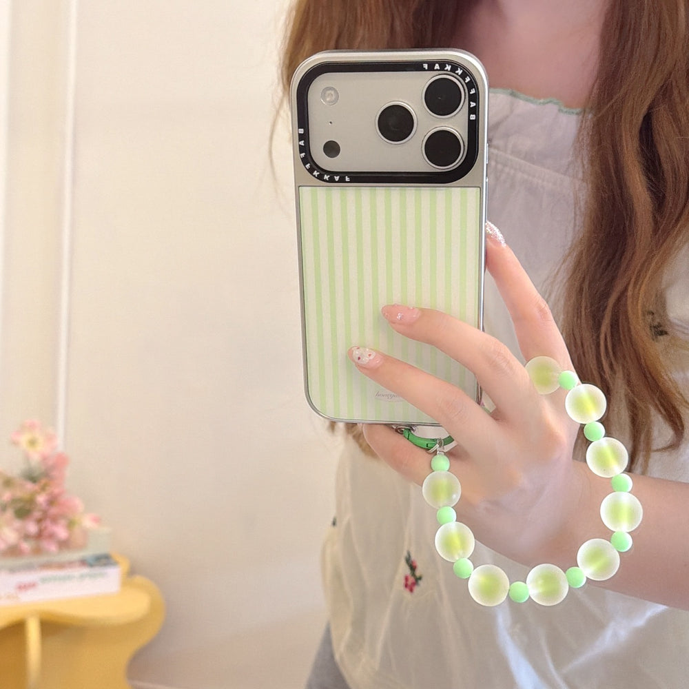 Close-up of a hand holding a kawaii green striped iPhone case featuring a silver lens frame and a matching wristlet.