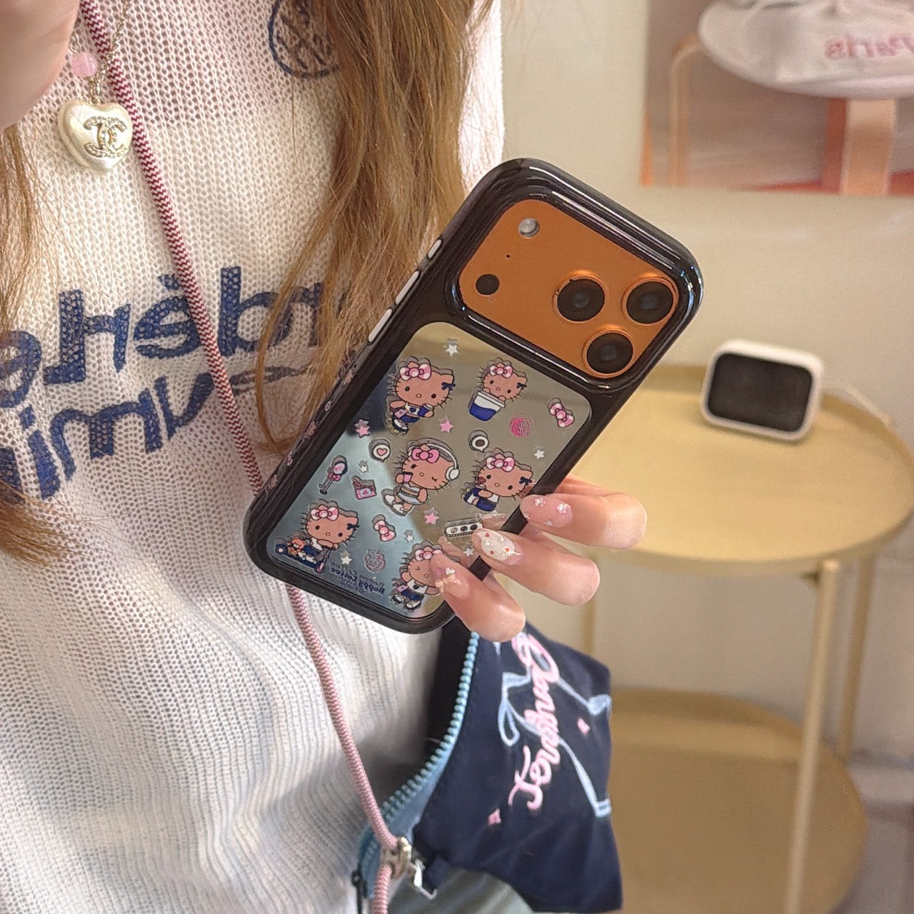 A woman holding a cute Hello Kitty mirror iPhone case with a vibrant orange camera protection frame.