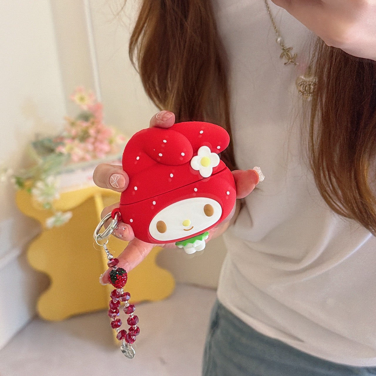 A woman holding a cute 3D silicone My Melody strawberry AirPods case with a red beaded keychain charm.