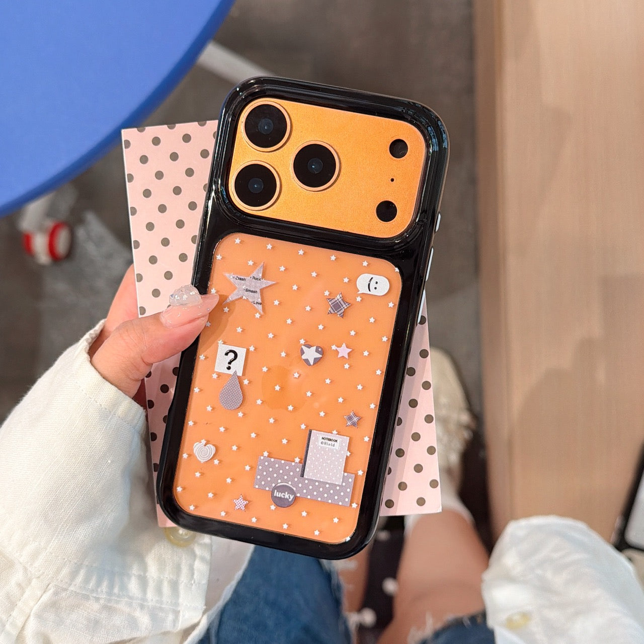 Close-up view of a kawaii orange mirror protective phone shell with cute doodle prints and full camera protection.