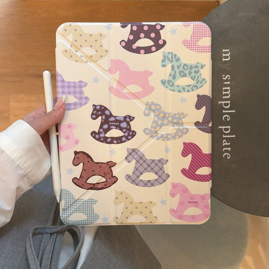 A handheld view of the closed front cover of a kawaii rocking horse ipad case in cream color, with a white stylus pen held on the left.