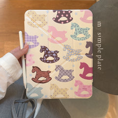 A handheld view of the closed front cover of a kawaii rocking horse ipad case in cream color, with a white stylus pen held on the left.