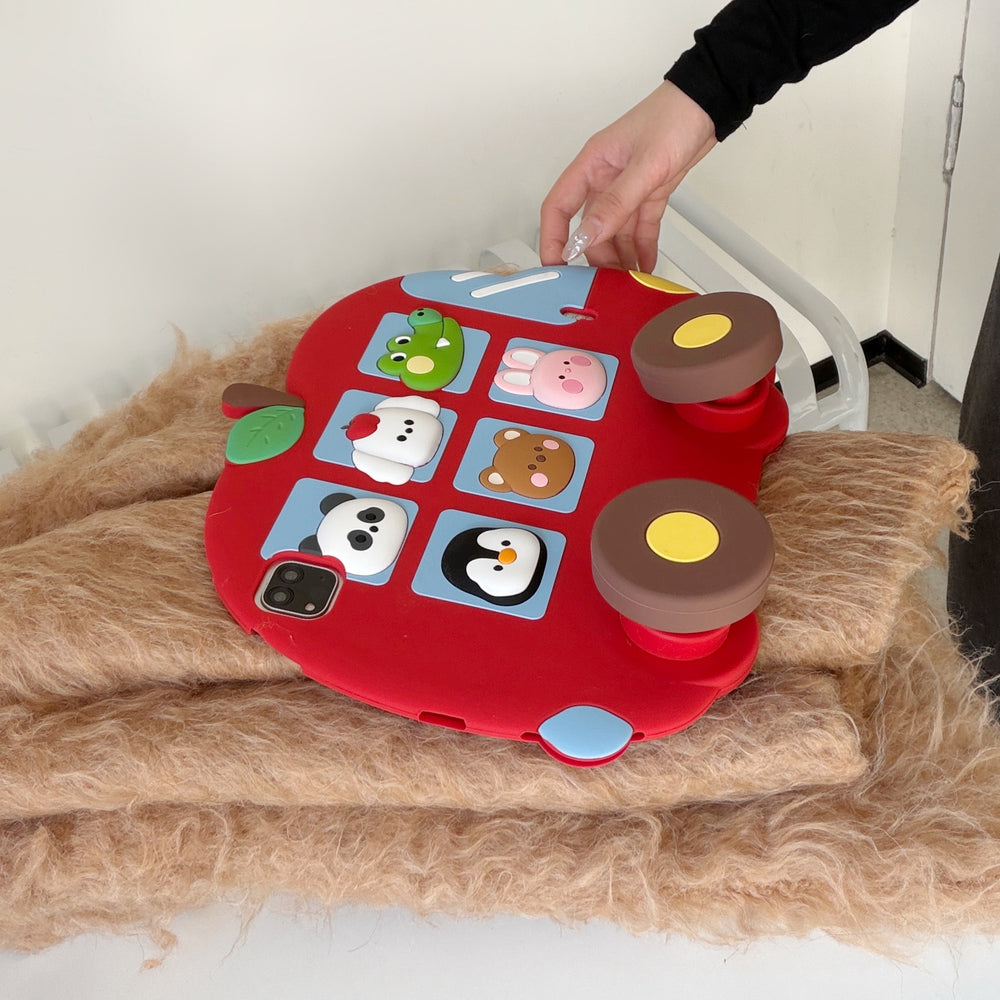 A close-up shot of the kawaii silicone iPad shell lying on a fluffy brown blanket, with a hand adjusting one of the two prominent brown wheel kickstands on the back.