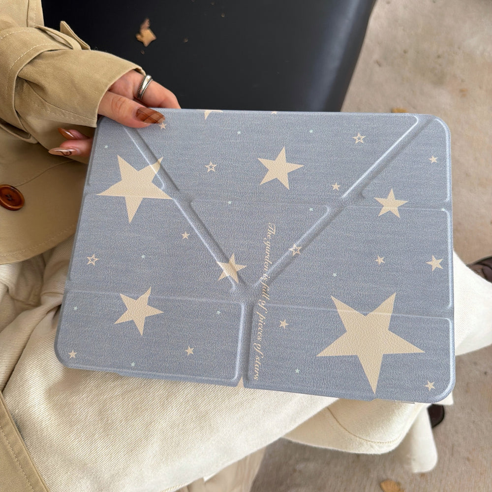 A closed kawaii starry sky origami iPad cover with geometric folding lines resting on a person's lap wearing a beige coat.