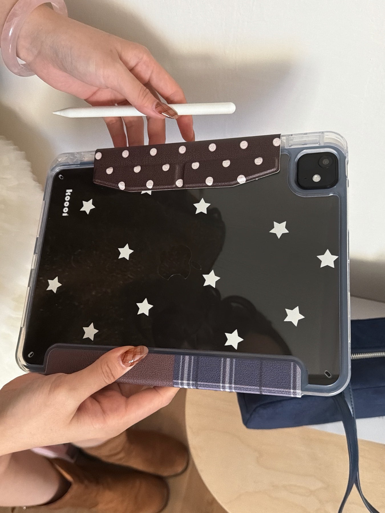 Hands holding the back panel of a Koooi aesthetic iPad case, displaying the printed white star patterns on a dark clear shell and a brown polka-dot magnetic flap.