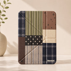 A minimalist studio shot of the Koooi vintage patchwork plaid iPad case standing upright on a beige surface next to a ceramic decorative plant vase.