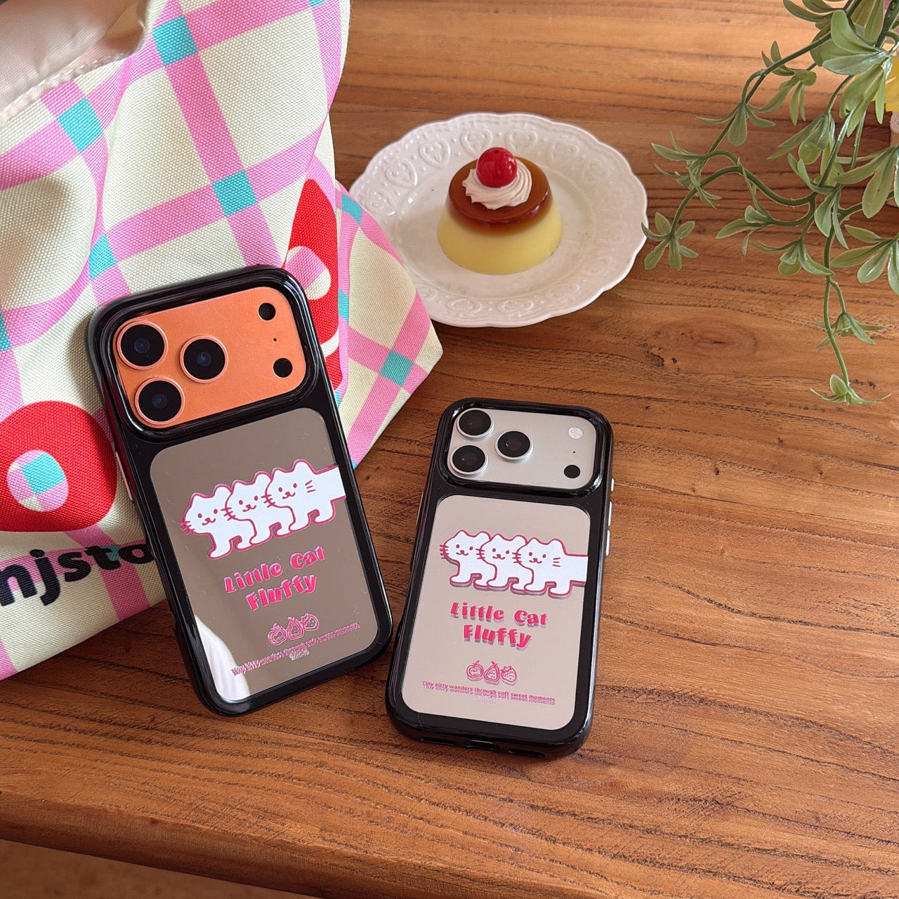 Flatlay layout of silver and orange Korean style mirror phone cases next to a plaid tote bag on a wooden table.