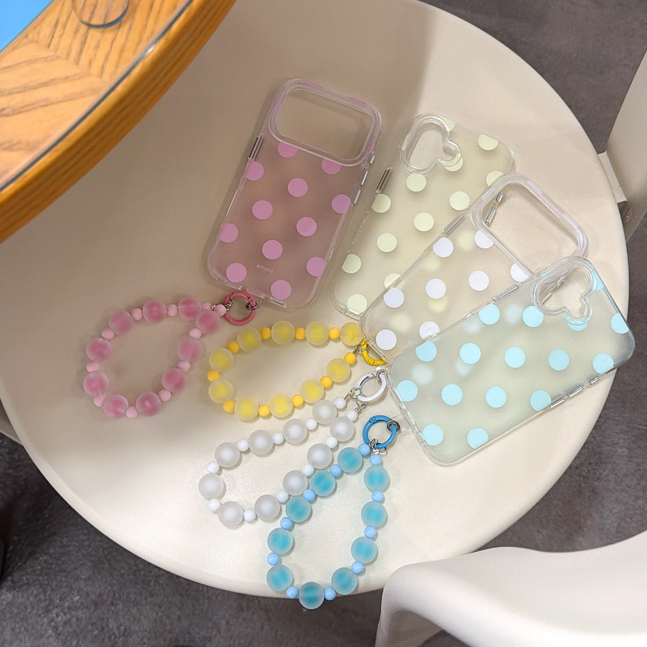 Four Korean style pastel polka dot phone cases arranged on a chair with colorful frosted bead wristlets.