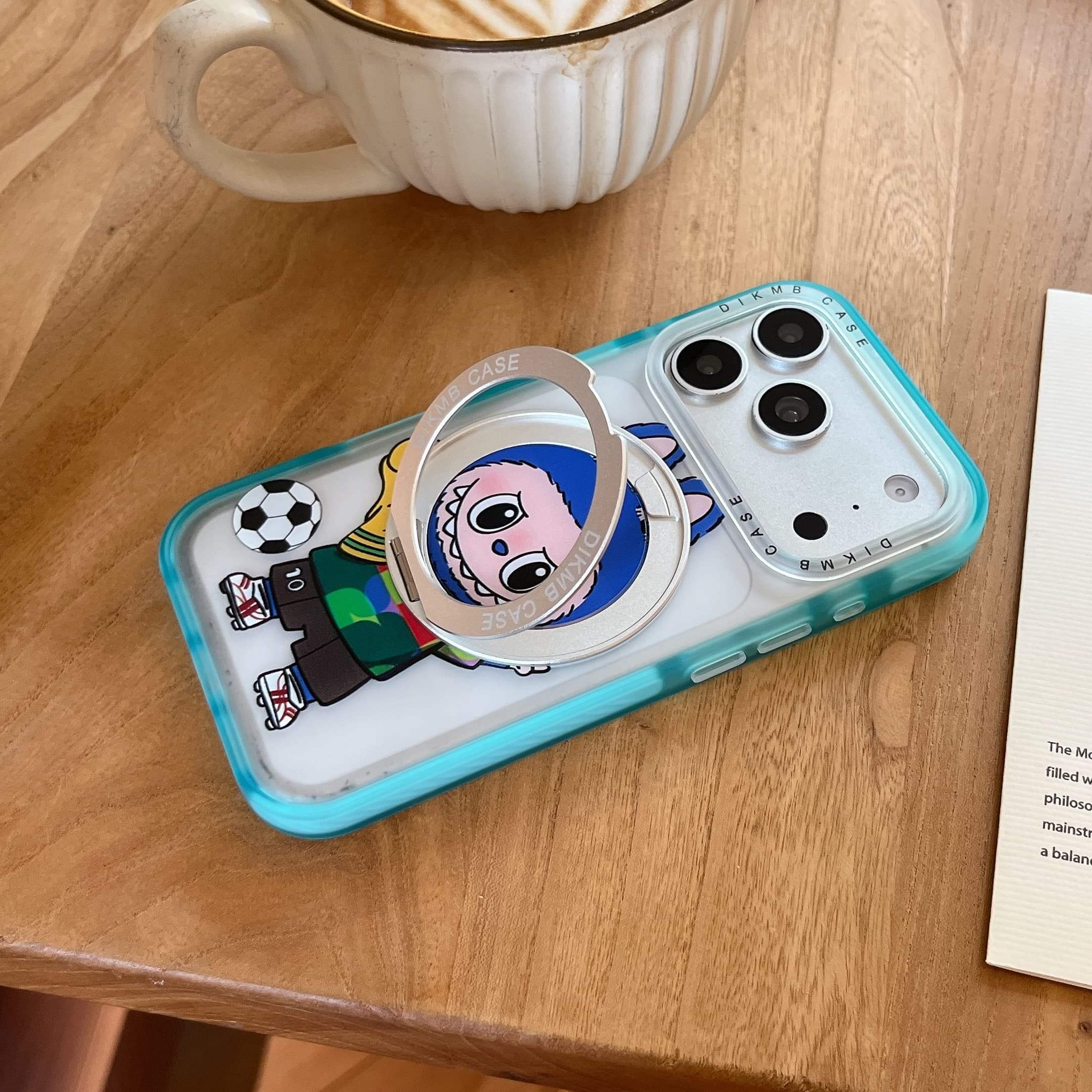 A Labubu cartoon phone case lying flat on a wooden coffee table next to a cup of hot latte.