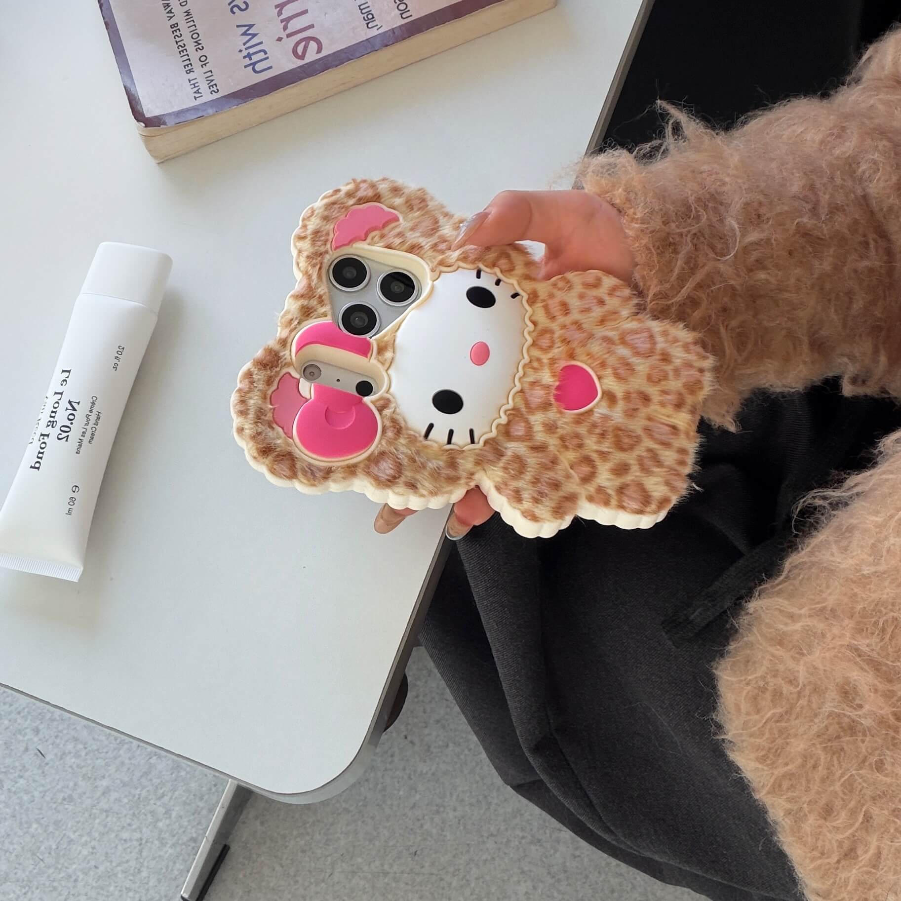 Leopard kitty plush iPhone case with a pink bow beside a table in a lifestyle setting