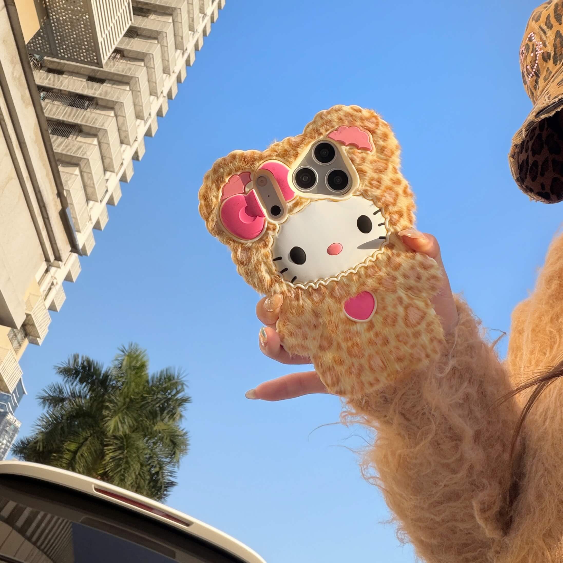 Leopard kitty faux fur iPhone case held outdoors against a blue sky