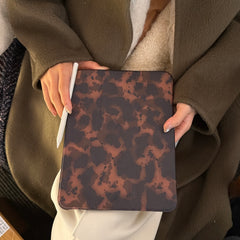 Close-up of a person holding a closed leopard print tri fold tablet case on their lap while gripping a white Apple Pencil, highlighting the sleek dark academia tech aesthetic.