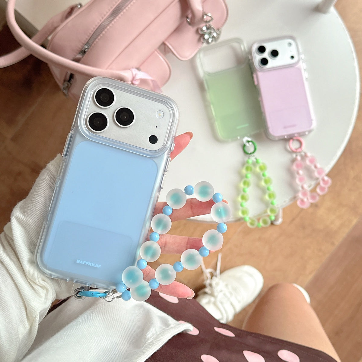 Top-down view of a hand holding a light blue matte phone case with a blue beaded charm over a polka dot dress.