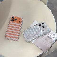 An orange and a silver striped phone case with cursive crystal Angel lettering placed on a cream white chair next to a book.