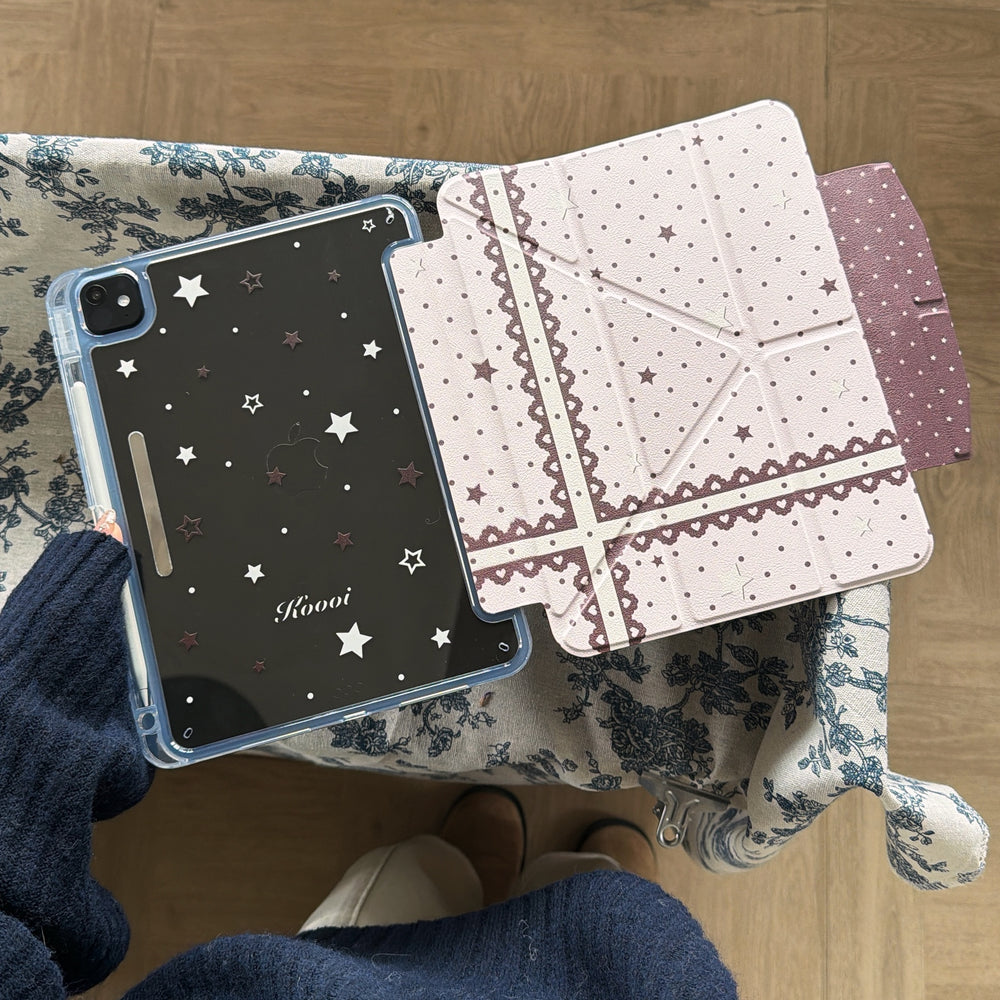 An open magnetic detachable coquette iPad case showcasing a clear back shell with star prints and a pink lace folio cover on blue floral cloth.