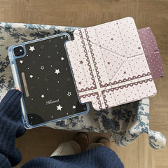 An open magnetic detachable coquette iPad case showcasing a clear back shell with star prints and a pink lace folio cover on blue floral cloth.