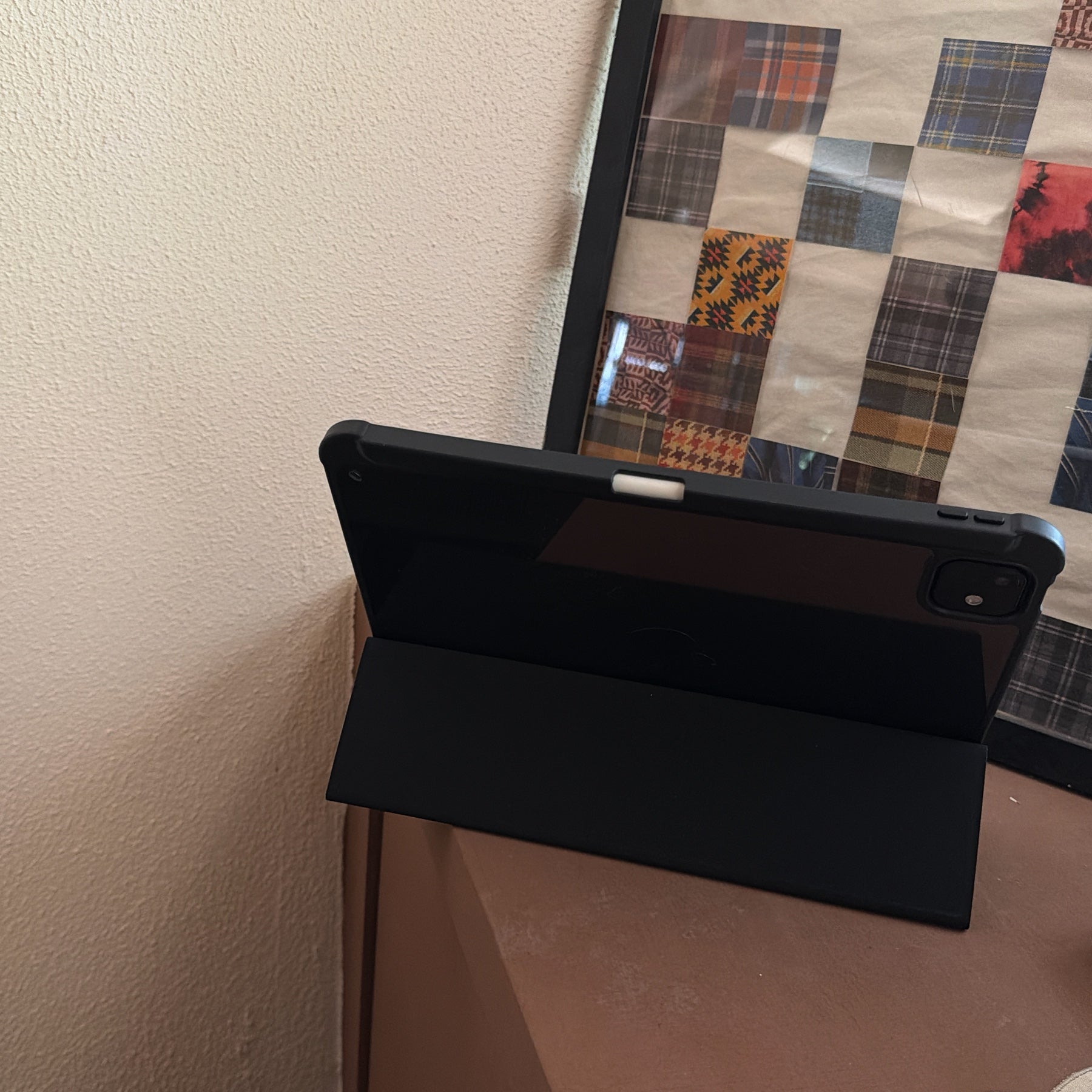 A magnetic detachable ipad case folded into a stable horizontal tri-fold smart stand on a wooden surface, next to a retro checkered picture frame.