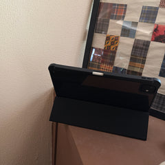 A magnetic detachable ipad case folded into a stable horizontal tri-fold smart stand on a wooden surface, next to a retro checkered picture frame.