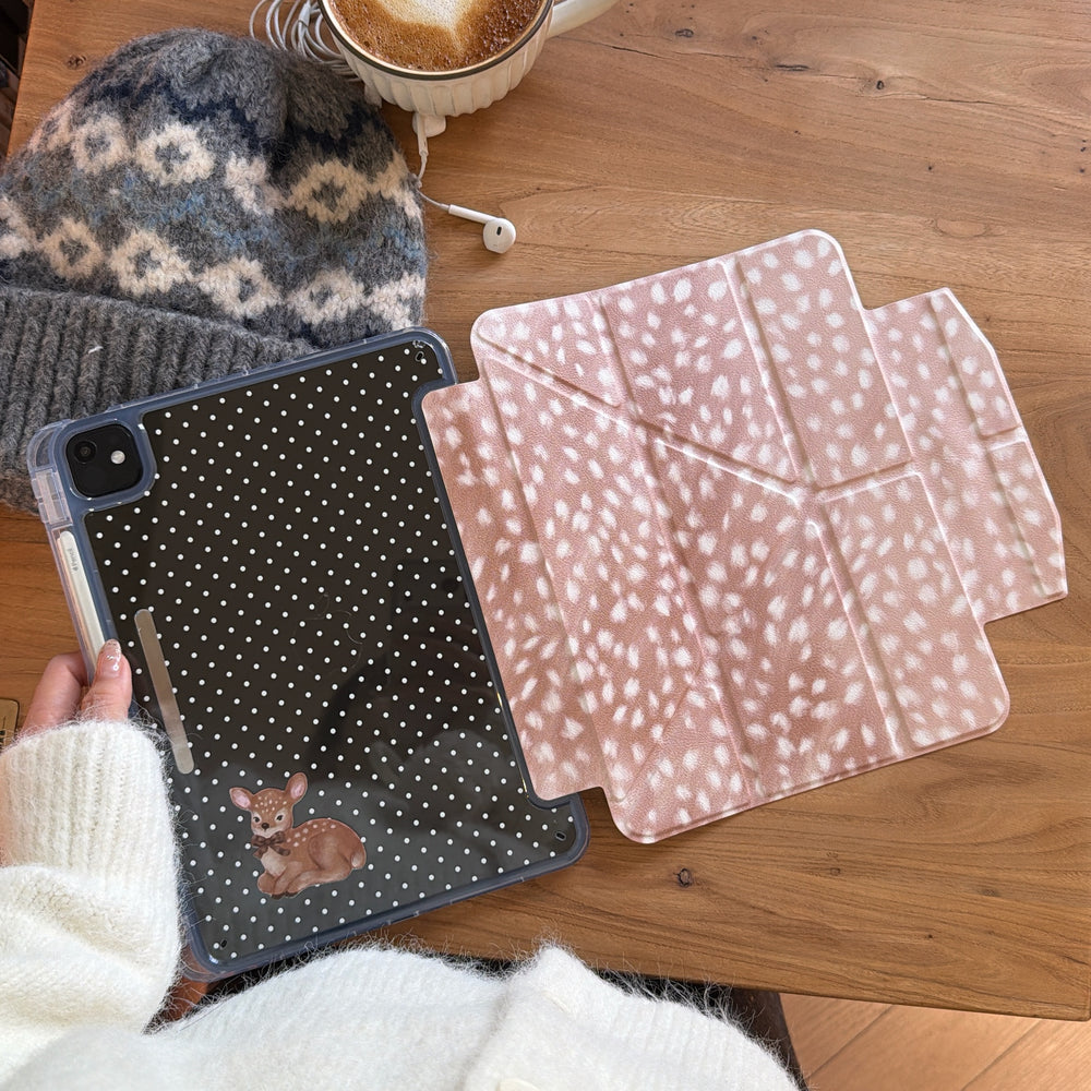 A cozy flat lay on a wooden table featuring a magnetic detachable vintage fawn iPad case separated into its polka dot back shell and deer-print origami folio, beside a warm latte and a knit beanie.