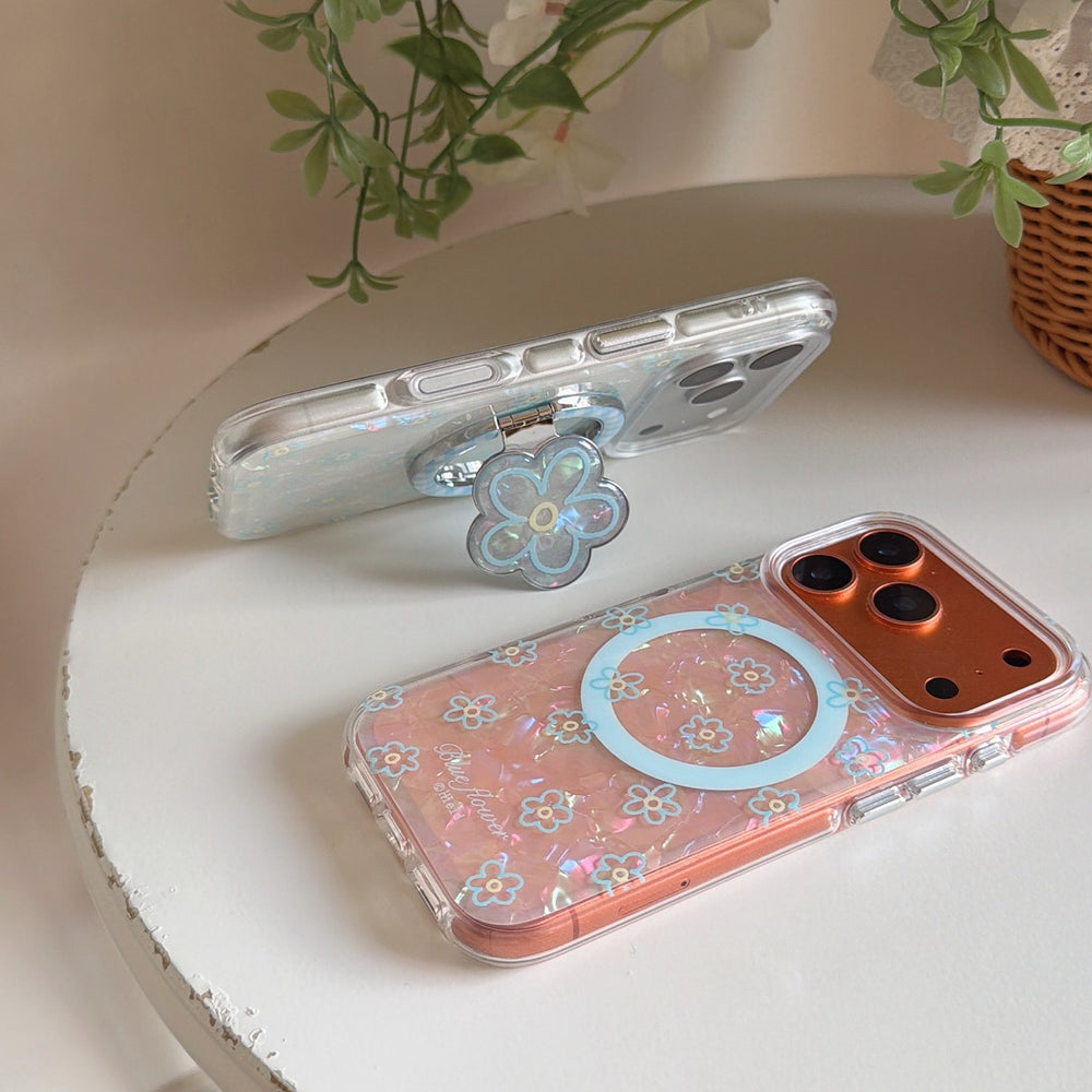 Two sparkling shell-texture phone covers—one with a flower kickstand and one with a MagSafe ring—on a white table.