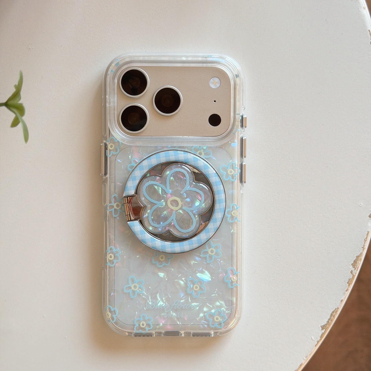 Product shot of an isolated clear magnetic iphone case with a built-in light blue MagSafe circle and aesthetic flower patterns.