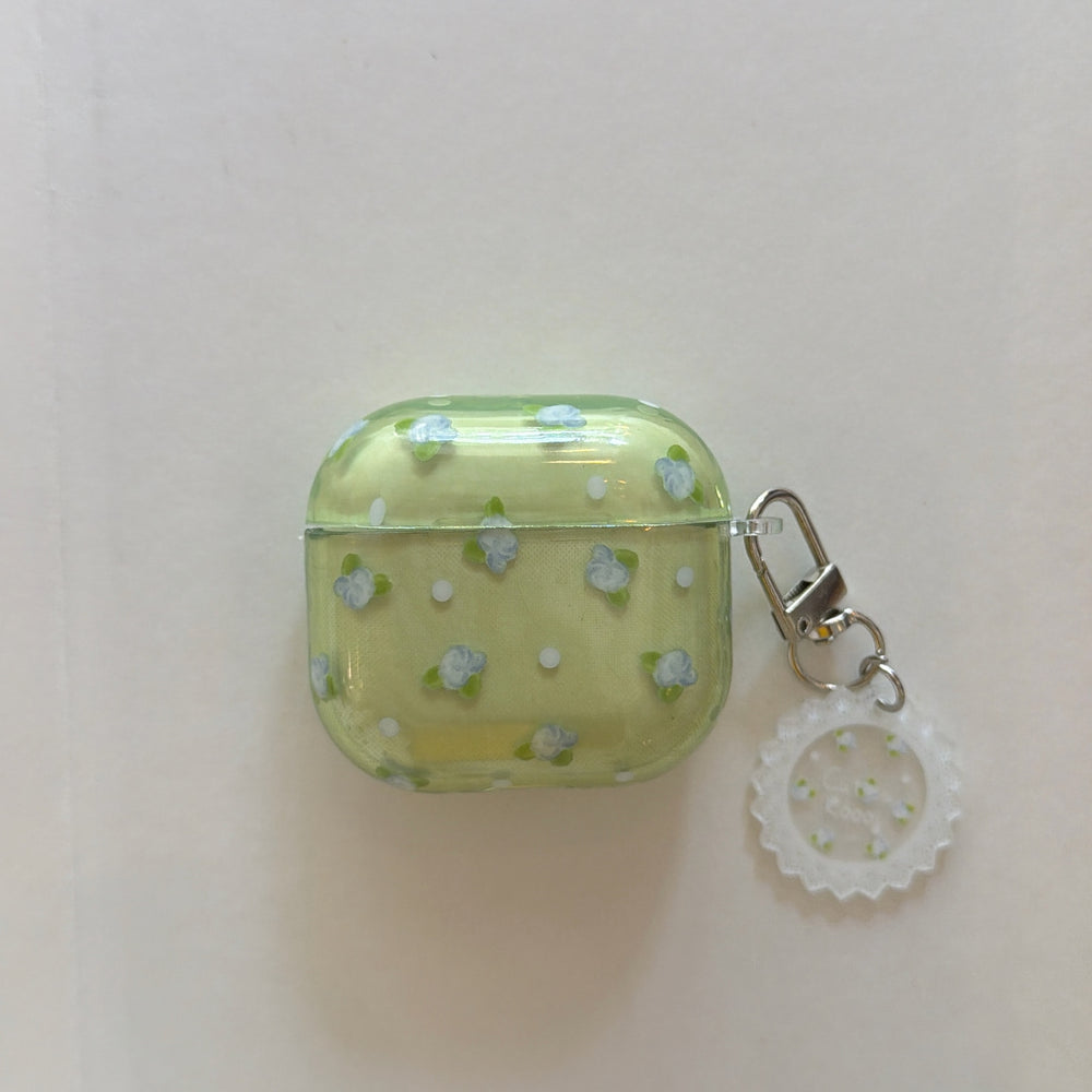 A translucent matcha green AirPods case with blue flowers, white polka dots, and a scalloped lace charm.