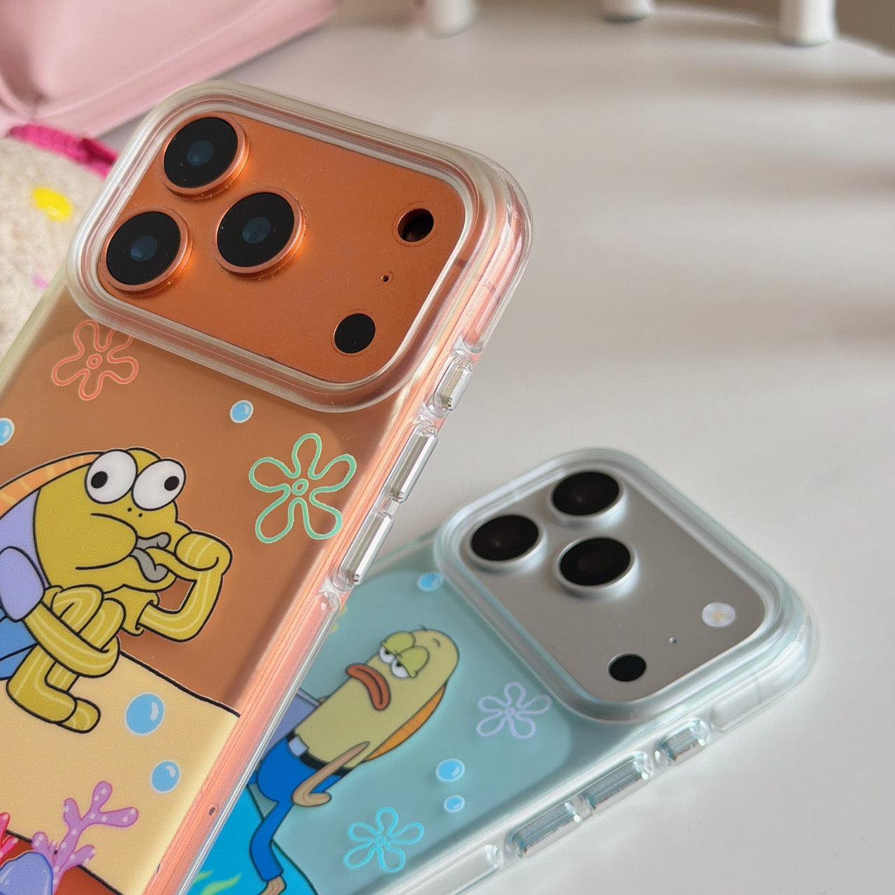 Close-up view of the glossy metallic camera deck protection frames on two clear cartoon phone cases.