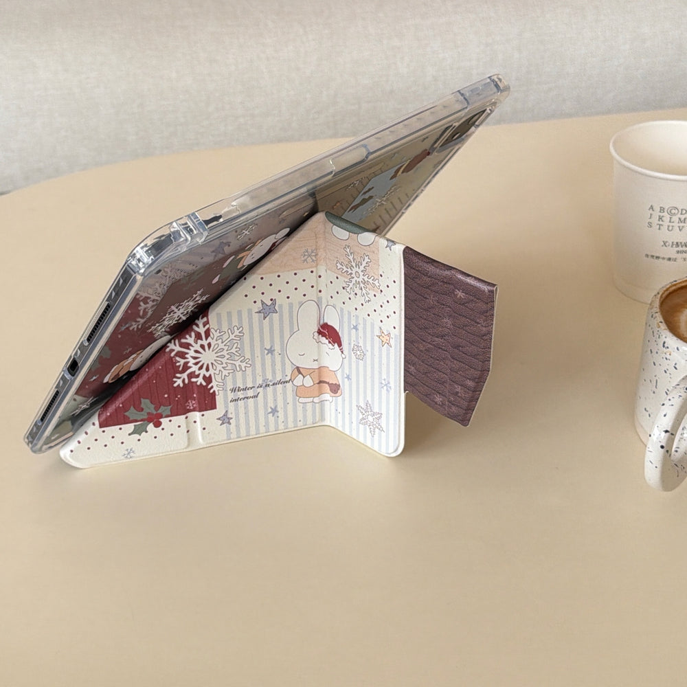 Side view of a kawaii Miffy iPad case folded into a stable origami stand on a beige desk, showcasing the cute winter bunny illustration on the smart cover.