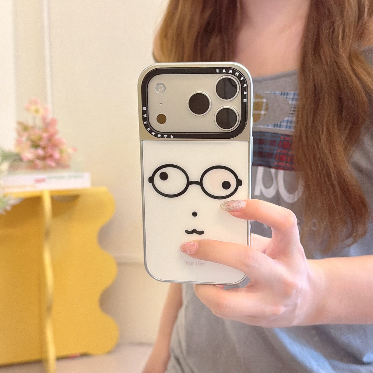 Close-up of a hand holding a minimalist glasses face iPhone case featuring a silver lens panel.
