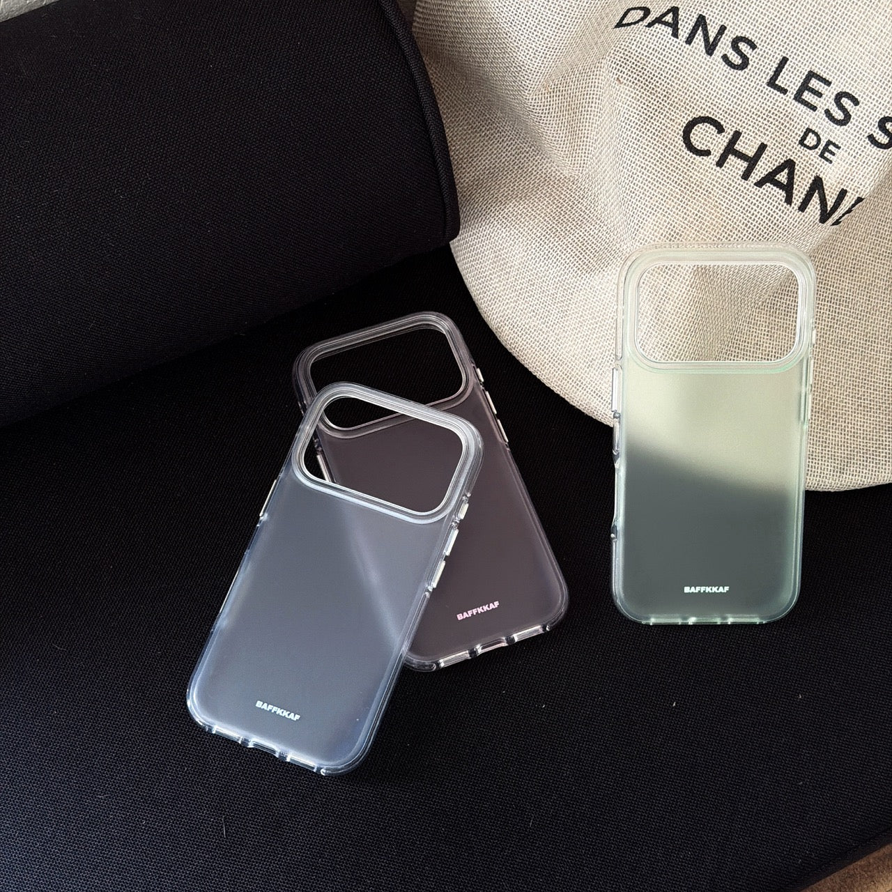 Three minimalist matte phone cases in blue, grey, and green displayed on a black surface next to a tote bag.