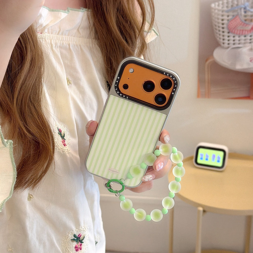 A girl holding a mint green striped iPhone case with a vibrant orange camera base and a green beaded wrist strap.