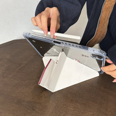 A close-up of hands adjusting a multi-angle magnetic iPad stand while attaching a white stylus pencil to the magnetic side of the clear acrylic shell.