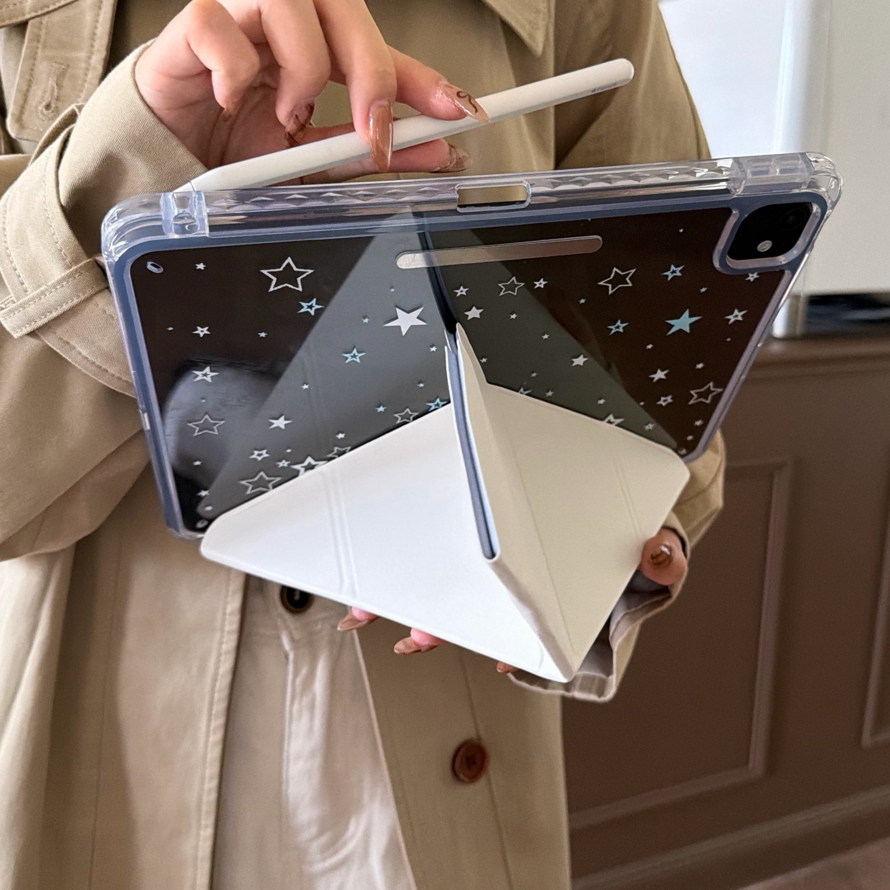 A person holding an Apple Pencil over an iPad propped up securely by a cream-colored multi-angle origami stand case.