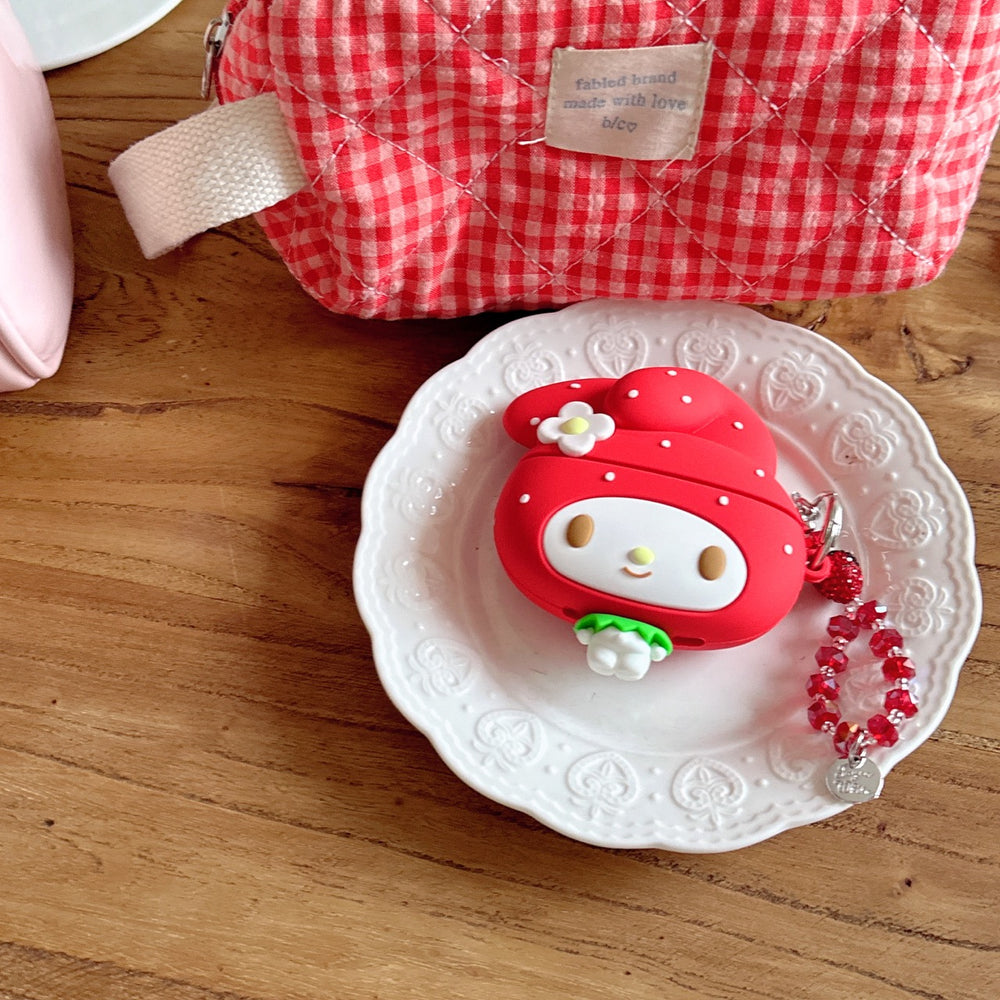 A cute red My Melody strawberry earbud charging case with a matching charm placed on a small white ceramic plate.
