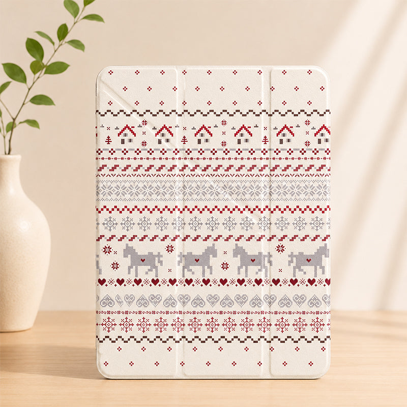 A closed cream-colored Nordic Fair Isle pattern iPad case standing upright on a light wooden table next to a white ceramic vase with green leaves.