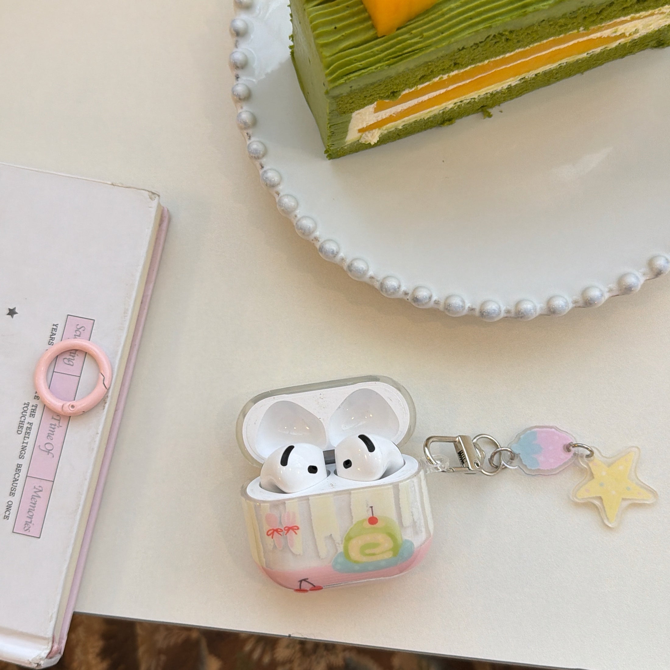 An open clear cake illustration AirPods case showing white earbuds inside next to a dessert plate.