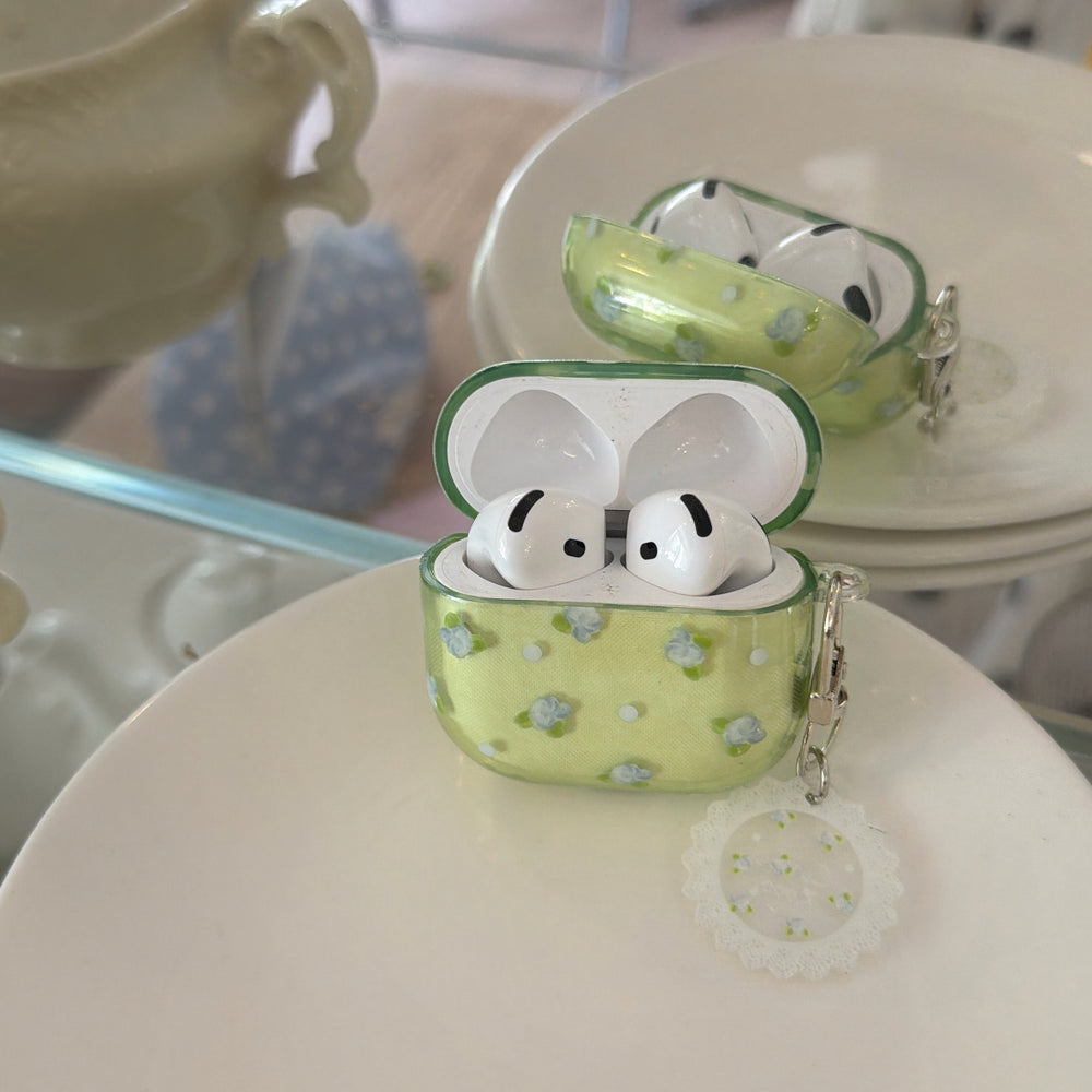 An open translucent green floral AirPods case with wireless earbuds inside, sitting on a white ceramic plate.