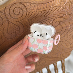 A hand holding an open kawaii cherry AirPods Pro case with both white earbuds nestled inside.