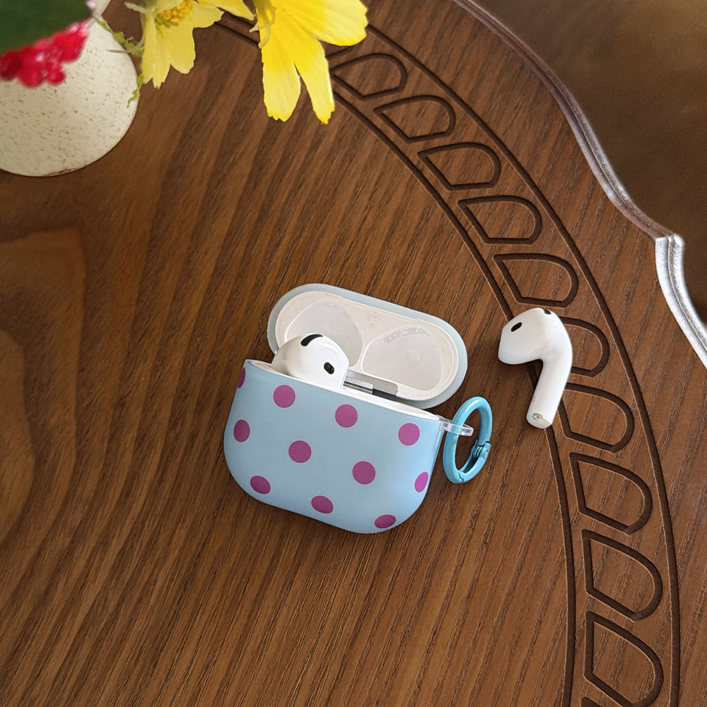 An open light blue polka dot AirPods Pro case with one earbud inside and one resting next to it on a carved wooden table.